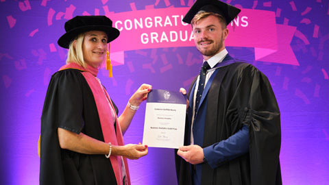 Two people in graduation attire; one hands a certificate to the other